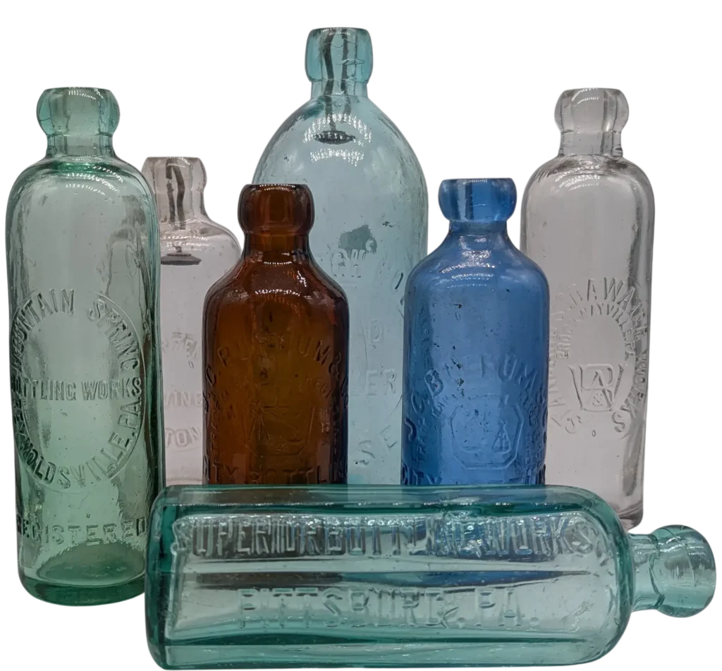 A Group of Seven Antique Blob Top Soda Bottles Arranged in a Row with One on its Side in the Front.